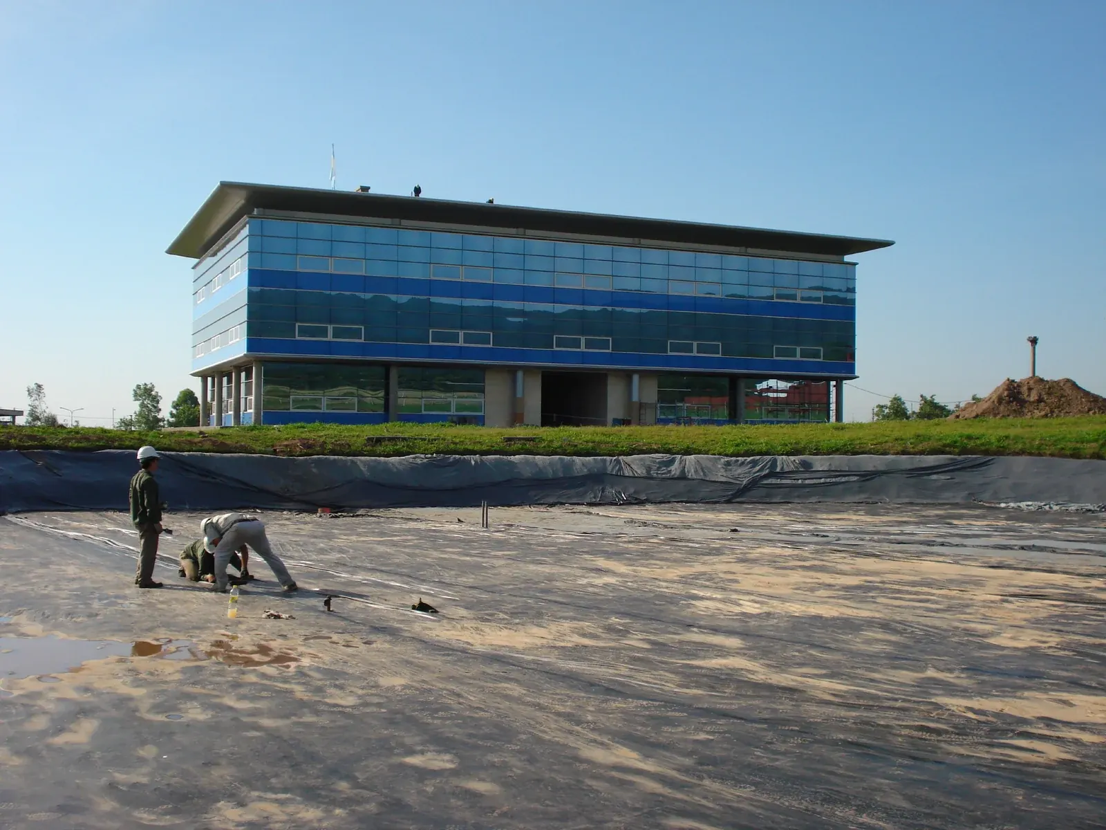 Preparación del terreno para impermeabilizar una laguna junto a un edificio corporativo